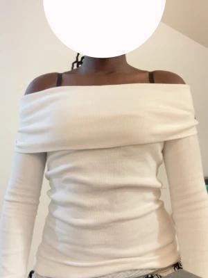 Vit offshoulder ribbad topp - Trendig vit offshoulder topp med lång ärm och ribbad struktur. Sitter tight och har en snygg, bred kant över axlarna. Perfekt för dig som vill ha en stilren och modern look.