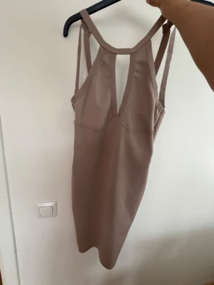 Beige kort klänning med smala band - Säljer en beige kort klänning med smala axelband och snyggt skuren rygg. Klänningen har en figurnära passform och är tillverkad i ett stretchigt material som ger en smickrande siluett. Perfekt för dig som gillar minimalistisk och stilren design.