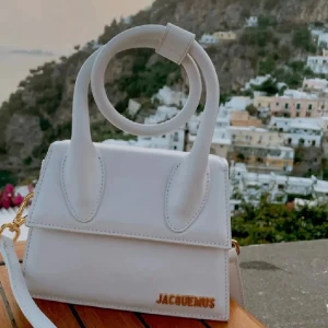Vit Jacquemus handväska i skinn - Superfin vit mini handväska med guldfärgad logga framtill. Väskan har ett runt handtag och en avtagbar axelrem.