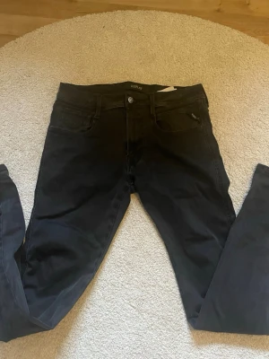 Svarta slim fit jeans från Replay - Snygga svarta slim fit jeans från Replay med klassisk femficksmodell och knappgylf. Jeansen har en modern passform och är tillverkade i ett stretchigt material för extra komfort. Perfekta för dig som gillar en stilren och enkel look.