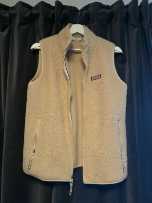 Beige ullväst - Mysig beige fleeceväst med hög krage och hel dragkedja framtill. Två fickor med dragkedja på sidorna och ett litet tygmärke på bröstet. Perfekt för lager-på-lager och chill dagar.