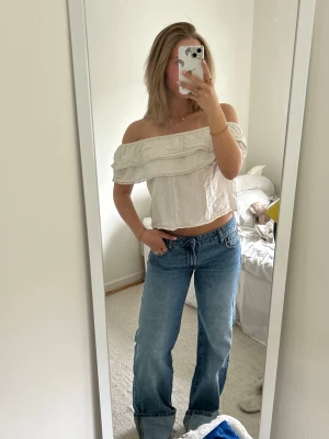 Vit offshoulder topp - Säljer en söt vit offshoulder topp med volangdetaljer och croppad passform. Toppen är ärmlös och har en luftig känsla, perfekt för varma dagar. Tillverkad i ett lätt bomullsliknande material och passar dig som gillar romantisk och trendig stil.