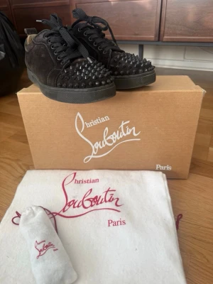 Svarta spikes-sneakers från Louboutin - Säljer ett par svarta sneakers från Christian Louboutin med coola svarta nitar/spikes över tån och snörning. Skorna är i mocka och i storlek 38 men skulle säga att de passar 39 oxå. Skorna är väl använda och saknar struktur under samt två stycken spikar (se bild 5) Trots välanvänd så är de i okej skick. Kommer med originalkartong och dustbag. Pris går absolut att diskutera! Kommer ej till användning därav säljer jag dom. 🌸 Skriv gärna vid funderingar! 💕