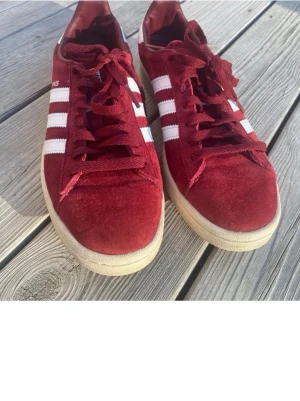 Adidas Campus röda sneakers - Riktigt snygga Adidas Campus sneakers i rött mocka med klassiska vita ränder på sidorna och vit sula. Lågt skaft och matchande röda skosnören. Perfekta för en streetwear-look och passar till det mesta.