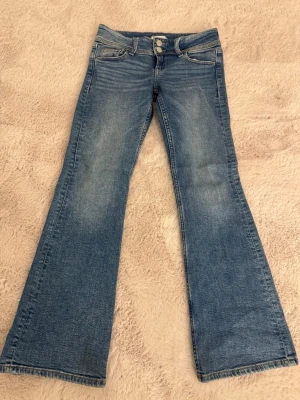 Blåa bootcut jeans - Snygga blå bootcut jeans med lätt slitning och dubbla knappar i midjan. Jeansen har framfickor och bakfickor med lock och knapp, samt klassiska sömmar. Köpt på Gina tricot (Young) 