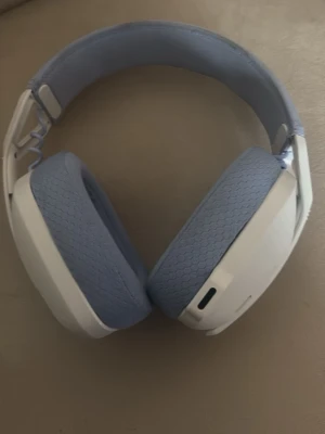 Vita och ljusblå gaminghörlurar - Snygga over-ear gaminghörlurar i vitt och ljusblått med mjuka, vadderade kuddar och justerbart huvudband. Hörlurarna har en modern design och är tillverkade i plast och tyg för extra komfort under långa spelsessioner.