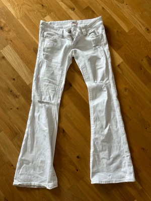 Vita bootcut jeans med slitningar - Säljer ett par vita bootcut jeans som är lågmidjade och har detaljer på bakfickorna 💕 Jeansen är i storlek S men passar tyvärr inte mig som i vanliga fall har den storleken. Skulle säga att de är mer Xs 🥰
