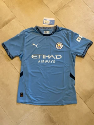 Manchester City matchtröja - Hej! Säljer en officiell Manchester City matchtröja från Puma. Den är i storlek L och är tillverkad i skönt och ventilerande funktionsmaterial. Den är aldrig använd och lappen sitter kvar. Perfekt för sommarens fotbollsäventyr! Tveka inte att höra av dig vid frågor!