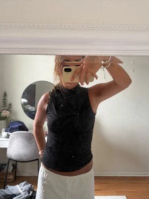 Svart ärmlös polotopp - Säljer en svart, tight polotopp utan ärmar. Toppen har hög hals och sitter figurnära, perfekt för att styla med olika underdelar. Enkel och stilren design som passar till många looks.
