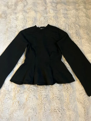 Svart långärmad topp med utsvängd midja - Svart långärmad topp med rund hals och utsvängd midja. Enkel och stilren design som passar till många olika looks.
