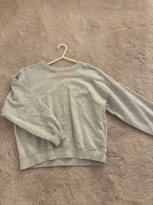 Grå sweatshirt - Enkel och stilren grå sweatshirt med rund halsringning och långa ärmar. Tröjan har ribbade muddar vid ärmslut och nederkant. Perfekt för en avslappnad och bekväm look. 