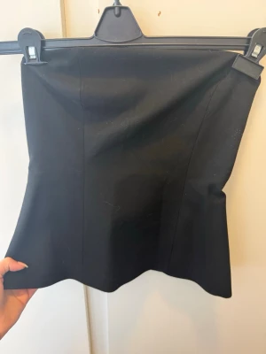 Svart axelbandslös tubtopp från Zara - Säljer en svart, axelbandslös tubtopp med figurnära passform. Toppen har en enkel och stilren design utan synliga detaljer eller mönster. Perfekt att styla med jeans eller kjol för en clean look.