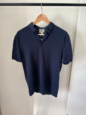 Mörkblå pikétröja  - En klassisk mörkblå pikétröja med korta ärmar och krage. Tröjan har knappar vid halsen och är tillverkad i mjukt bomullsmaterial. Perfekt för en avslappnad och stilren look.