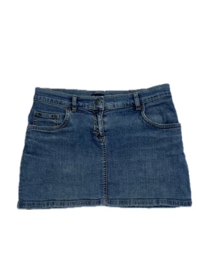 Blå jeanskjol i kort modell - Klassisk blå jeanskjol i kort modell med bälteshällor. Knappen+nitarna framtill har små stjärnor på. Kjolen har knapp- och dragkedjestängning framtill och raka sömmar. Stretchigt jeanstyg. Märke: att. Storlek: 38 