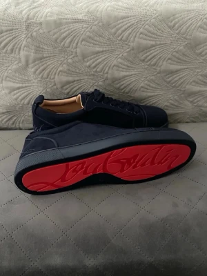Mörkblåa Christian Louboutins - Snygga mörkblå Christian Louboutins i mocka med klassisk låg profil och matchande mörkblå snörning. Insidan är beige och yttersulan är röd med ett coolt mönster. Perfekta för dig som vill ha något stilrent men ändå sticker ut.