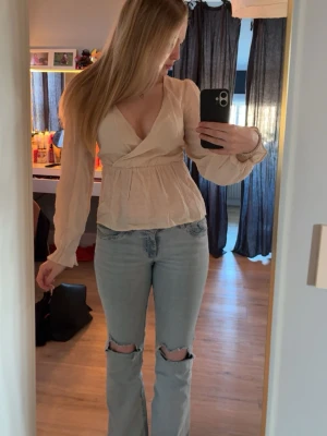 Beige omlottblus från Vero Moda - Säljer en beige omlottblus från Vero Moda i storlek S. Blusen har lång ärm, v-ringning och en lätt rynkad midja som ger en snygg siluett. Tillverkad i ett tunt, luftigt tyg. Perfekt för dig som gillar en stilren och fräsch look.  Inte använt den en enda gång, så splitterny😊🤍