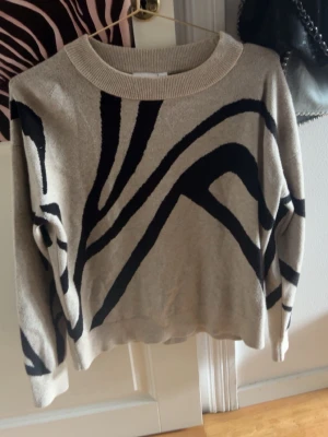 Beige stickad tröja med zebramönster - Stickad tröja från Vila i beige med svart zebrainspirerat mönster. Tröjan har rund halsringning och ribbade muddar. Perfekt för dig som gillar djurmönstrat och vill ha en trendig look.