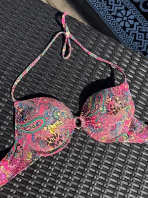 Snygg bikiniöverdel - Snygg bikiniöverdel i starka färger med paisleyinspirerat mönster i rosa, gult och turkost. Bikinin har vadderade kupor, knyt i nacken och en liten ringdetalj framtill🩷💛🩵