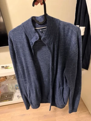 Blå stickad kofta  - Mysig blå stickad kofta från ollygan  med ståkrage och knappar vid halsen. Koftan har långa ärmar och två fickor framtill. Perfekt för lager-på-lager och enkel att matcha med jeans eller chinos.