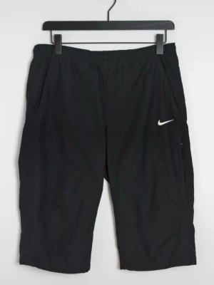 Svarta träningsshorts från Nike - Svarta träningsshorts från Nike med elastisk midja och diskret vit logga på ena benet. Shortsen har sidofickor och är tillverkade i ett lätt och funktionellt material som passar perfekt för sport och aktivitet.