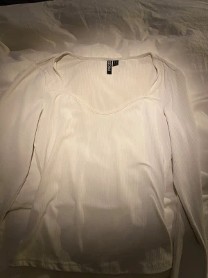 Vit ribbad topp från Pieces - Säljer en vit långärmad topp från Pieces med ribbad struktur och en snygg, något djupare rundad urringning. Materialet är stretchigt och följsamt. Enkel men stilren design som passar till det mesta. 