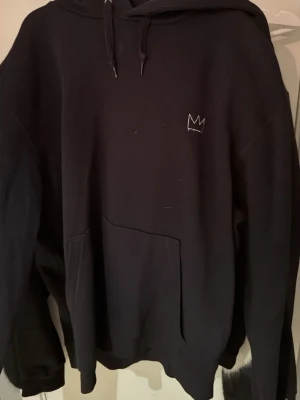 Svart Hov1 hoodie med turnétryck - Svart hoodie från Hov1 med liten krona broderad på bröstet och stort turnétryck på ryggen. Klassisk känguruficka framtill och justerbar huva med snören. Perfekt för dig som gillar svensk hiphop och vill ha en snygg och bekväm hoodie.
