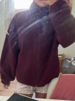 Vinröd teddyjacka med dragkedja - Mysig vinröd teddyjacka med hög krage och hel dragkedja framtill. Jackan har en oversized passform och är tillverkad i fluffigt teddy-material som håller dig varm. Perfekt för lager-på-lager och chill dagar.