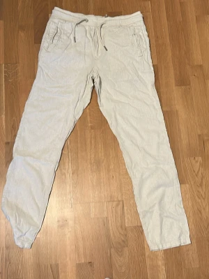 Beiga linnebyxor med dragsko - Snygga och avslappnade beiga linnebyxor med dragsko i midjan och sidofickor. Perfekta för en chill och stilren look. Lätta och luftiga, passar grymt till sommaren. Raka ben och enkel design utan synligt märke.