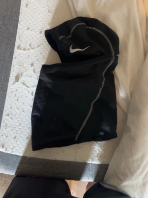 Svart Nike sporthuva med sömmar - Svart sporthuva från Nike med vit logga och kontrasterande grå sömmar. Perfekt för träning utomhus eller löpning när det är kallare. Tillverkad i ett stretchigt och lätt material som andas.