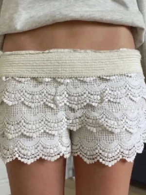 Spetshorts - Superfina ljus beiga shorts med spets och volangdetaljer. De har en bred, elastisk midja och ett lager-på-lager mönster med små bollar längs kanterna. Perfekta för en somrig look och riktigt sköna att bära.