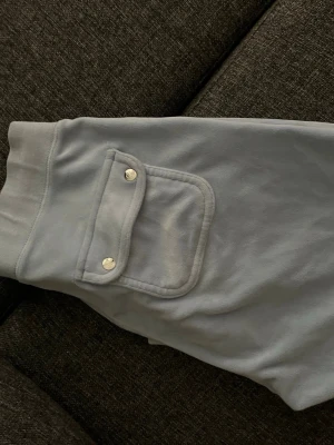 Ljusgrå mjukisbyxor med fickor - Snygga ljusgrå mjukisbyxor med bred resår i midjan och dragsko med metalländar. Byxorna har stora fickor fram och en ficka bak med lock och tryckknappar. Perfekta för en chill och avslappnad stil.