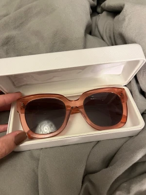 Rosa solglasögon från Chimi - Säljer ett par snygga solglasögon från Chimi i transparent rosa plast med mörka glas. Modellen har en klassisk, rak form och diskret logga på sidan. Perfekta för dig som vill ha en trendig accessoar med lite färg.