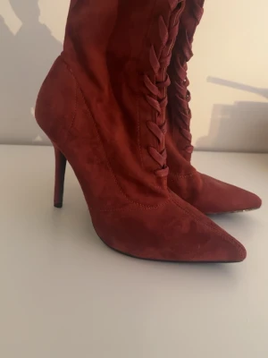 Vinröda spetsiga stövletter med snörning - Snygga vinröda stövletter med spetsig tå och hög smal klack. Skorna har dekorativ snörning framtill och är tillverkade i ett mockaliknande material som ger en lyxig känsla. Perfekta för dig som vill sticka ut med din stil.