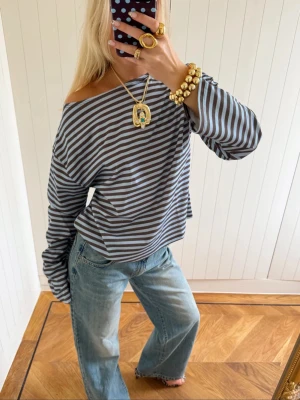 Randig off shoulder topp - Aldrig använd topp. Snygg randig topp i grått och blått med offshoulder-design och lång arm. Tröjan loose passform som ger en avslappnad vibe. Perfekt att styla med jeans för en cool look.