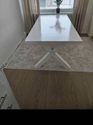 Vitt matbord med kryssben - Stilrent vitt matbord med rektangulär bordsskiva och snygga kryssben i trä. Bordet har en modern design och passar perfekt i köket eller matsalen. Bordsskivan är slät och reflekterar ljuset fint.