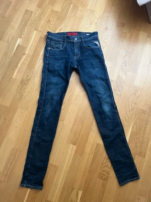 Mörkblå skinny jeans från Replay - Snygga mörkblå skinny jeans från Replay med klassisk femficksdesign och diskreta slitningar. Jeansen har smal passform och kontrastsömmar, samt läderpatch med logga bak i midjan. Perfekta för en trendig och avslappnad stil.