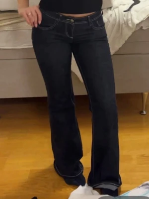 Mörkblå bootcut jeans med kontrastsömmar - Säljer ett par mörkblå bootcut jeans med vita kontrastsömmar och klassisk femficksdesign. Jeansen har låg midja och utsvängda ben. Jag är 170cm och dom är perfekt i längden. Jeansen är i storlek 32 men passar mig som i vanliga fall har 34, pris går att diskuteras🤗