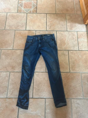 Mörkblå slim fit jeans från replay - Snygga mörkblå slim fit jeans från replay med klassisk femficksdesign och subtila slitningar. Jeansen har en smal passform och är tillverkade i ett mjukt denimtyg som ger en bekväm känsla. Perfekta för dig som gillar en stilren och modern look. 31/32