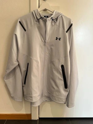 Ljusgrå vindjacka från Under Armour - Knappt använd ljusgrå/blå vindjacka från Under Armour. I perfekt skick. Storlek: M. Tveka inte på att höra av dig vid frågor eller bilder!! 
