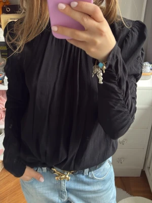 Svart blus med puffärm och veck - Svart blus med långa puffärmar och fina veck framtill. Blusen har en lös passform och är tillverkad i ett lätt, mjukt tyg som ger ett elegant fall. Perfekt att styla med jeans eller kjol för en trendig look.