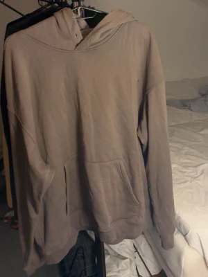 Beige oversized hoodie - En enkel beige hoodie med huva och känguruficka framtill. Hoodien har en avslappnad, oversized passform och ribbade muddar vid ärmar och nederkant. Perfekt för en chill och casual look. Materialet känns mjukt och bekvämt, troligen bomull eller bomullsblandning.