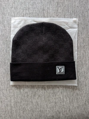 L och v - Snygg svart mössa  med diskret rutmönster och uppvikt kant. Märkets klassiska sitter framtill på en patch. Perfekt accessoar för att lyfta din streetstyle. Materialet är stickat och känns mjukt