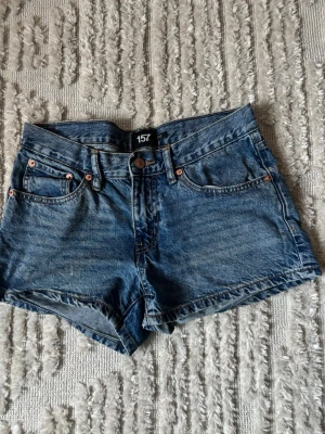 Blå jeansshorts från 157 - Säljer ett par klassiska blå jeansshorts från 157 med fem fickor och knappgylf. Shortsen har en tidlös denimlook och är perfekta för varma dagar. Passar dig som gillar enkel och avslappnad stil.