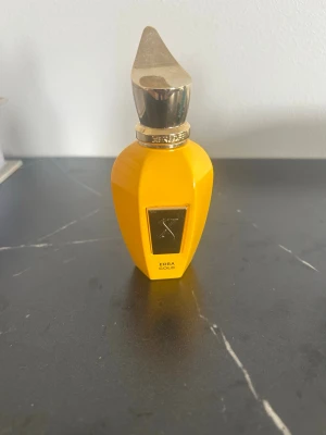 Xerjoff Erba Gold parfymflaska - Snygg parfymflaska från Xerjoff i modellen Erba Gold. Flaskan är klargul med guldiga detaljer och har en unik, spetsig kork i guld. Flaskan är tillverkad i glas och har en exklusiv känsla med geometrisk form. Endast 40/50 ml kvar