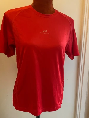 Röd tränings-tshirt från Peak Performance M - Denna kortärmade t-shirt är designad för en bekväm passform. Tröjan har en rund halsringning och korta ärmar, vilket gör den lämplig för olika aktiviteter. Den röda färgen ger ett klassiskt utseende. Längd: 65 cm, Bystvidd: 48 cm Polyester Uppskattad storlek M  Inga bilder på mig! Katter finns i hemmet!