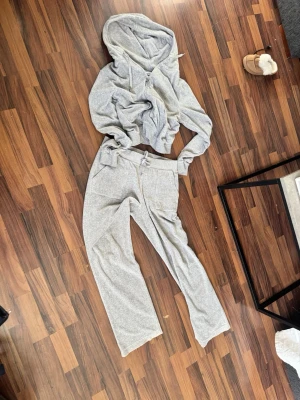 Grått loungewear-set med hoodie - Mysigt loungewear-set i ljusgrått med mjuk hoodie och matchande byxor med dragsko i midjan. Hoodien har dragkedja och byxorna har raka ben och fickor. Perfekt för chill dagar hemma. Från Juicy Couture är en lite fläck back på byxorna det va så när jag köpte dom stolen m på båda delar 