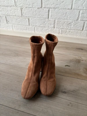 Bruna stövletter med blockklack - Snygga bruna stövletter i mocka-look med höga skaft och bred blockklack. De har en stilren design med sömdetaljer framtill och är perfekta för att lyfta din outfit. Materialet är mjukt och ger en cool vibe.