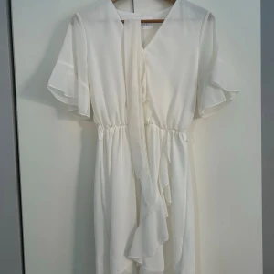 Vit klänning  - Superfin vit omlottklänning från Sisters Point med v-ringning, volangdetaljer och korta, fladdriga ärmar. Klänningen har knyt i midjan och är i ett lätt, flowy material som känns luftigt och fräscht. Perfekt till sommarens alla tillfällen!