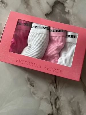 Trosor från Victoria's Secret i 4-pack - Säljer ett 4-pack ribbade trosor från Victoria's Secret i färgerna vit, ljusrosa och ceriserosa. Trosorna har bred resår med logotyp och fina spetsdetaljer längs kanterna. Perfekt för dig som gillar både komfort och snygg design.