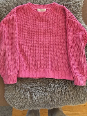 Rosa stickad tröja från H&M - En chunky rosa stickad tröja från H&M med rund halsringning och långa ärmar. Tröjan har ett grovt stickat mönster och ribbade muddar vid ärmslut och nederkant. Perfekt för att skapa en färgstark look.